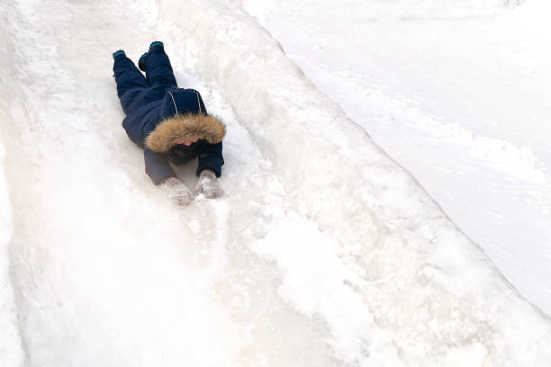 istock A child in winter clothes, cheerfully rolls down lying on his stomach, face forward, from a snowy mountain in winter. 1288343268