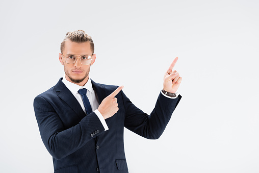 young businessman in suit and glasses pointing up isolated on white