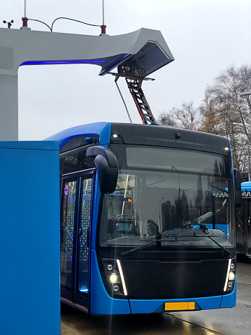 Blue electric bus is charged by pantograph at the station