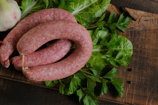 Sausage ring, garlic, chard and parsley, on brown wooden board on wooden table background.Meats and Sausages.Top view. Homemade natural sausage.