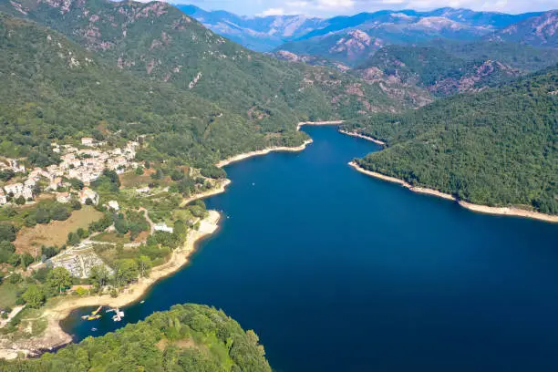 Photo of Lake Tolla Corsica and the mountain village of the same name. Deep green trees surround the blue lake with its crystal clear water.