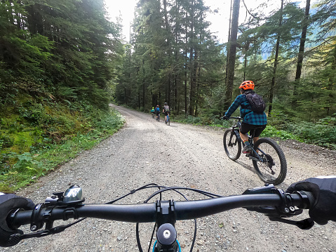 Personal perspective of multi-ethnic family riding mountain bikes on gravel road through forest.  North Vancouver, British Columbia, Canada.
