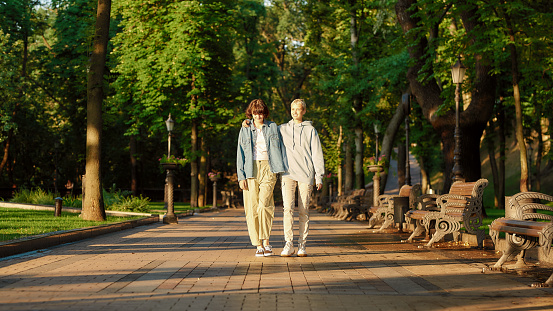 Full length shot of lesbian couple having a date in the city park. Two women spending time together, admiring sunny day while walking outdoors. Homosexuality, LGBT and love. Front view. Web Banner