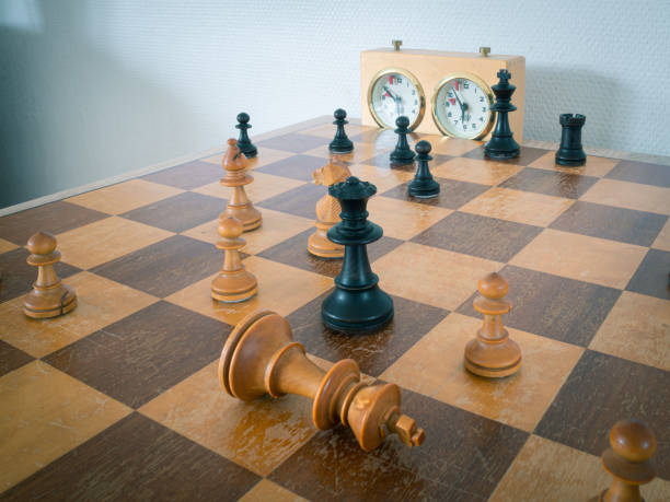 White king and black queen in a game of chess Chessboard with pieces. White has resigned and placed his king flat on the chessboard. chess timer stock pictures, royalty-free photos & images