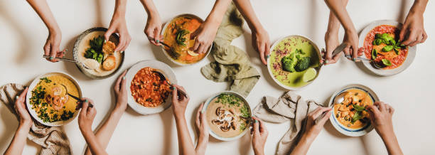 Flat-lay of peoples hands with soup plates and bread slices People eating Autumn and Winter creamy vegan soups. Flat-lay of peoples hands with soup plates and bread slices over plain white table background, top view. Fall and Winter food menu, vegetarian food comfort food stock pictures, royalty-free photos & images