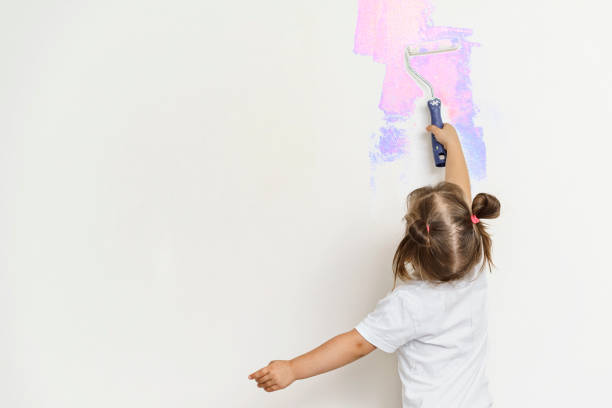 child paints the wall with a roller cute little girl paints the gray wall with a construction roller in bright colors better world stock pictures, royalty-free photos & images