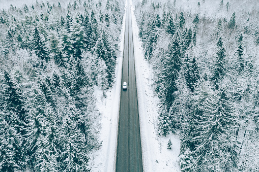 Aerial view of winter road with a car and snow covered trees in the forest