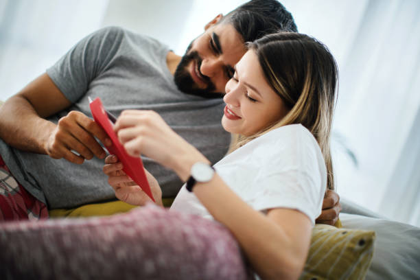 Our wedding invitation is perfect. Young couple enjoying morning in the bed. They are happy because their wedding invitation has arrived and they are happy with how it looks. love message stock pictures, royalty-free photos & images