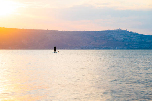 o homem navega em uma prancha sup em um grande lago durante o nascer do sol. stand up paddle boarding - recreação ativa na natureza - lake tiberius - fotografias e filmes do acervo
