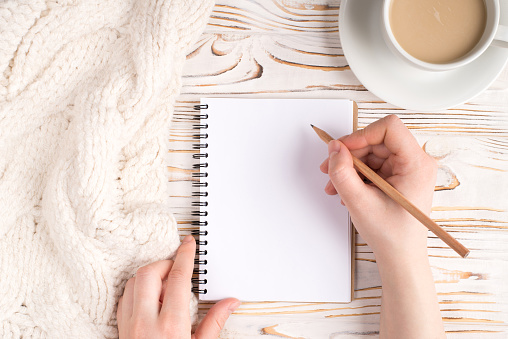Writing check list concept. Pov top above overhead close up view photo of female hand making notes in empty notepad near white plaid and hot cup of coffee