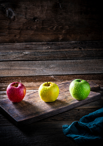 Colorful three apples in a row red golden and green apple on rustic wooden background over cutting board