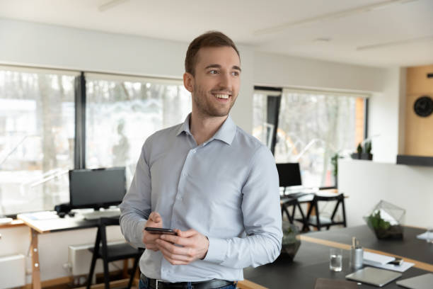 istock Smiling millennial businessman holding smartphone in hands. 1288409405