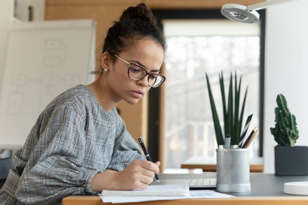 istock Focused young african american employee writing notes in copybook. 1288409415