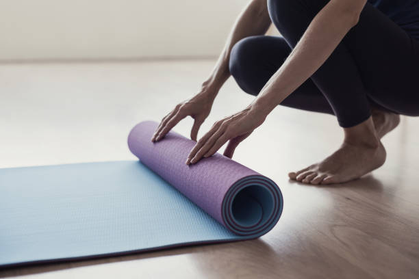 donna che arrotola il tappetino da allenamento e si prepara a fare yoga o fitness - materassino foto e immagini stock