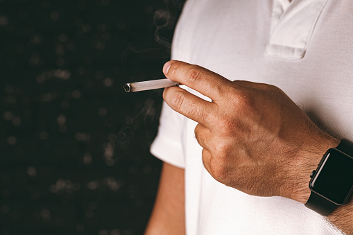Male hand holding lit cigarette against black background close up