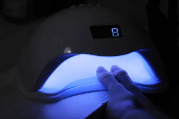 Closeup view of female hands with gel polish manicure. Woman puts hand into led uv lamp for curing top cover of nailpolish. UV lamp, LED Nail.