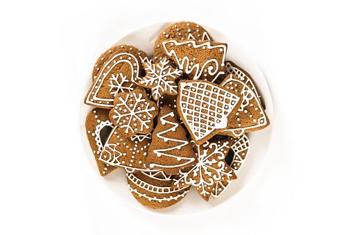 Various gingerbread cookies in different shapes - Christmas tree, star, bell, snowflake, heart etc. on a plate isolated on white background.