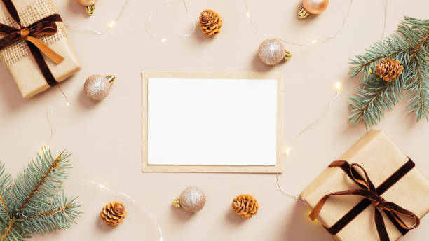 istock Christmas composition. Feminine table with blank paper card mockup, gift boxes, fir tree branches, balls, garland on pastel beige background. Flat lay, top view. Nordic, hygge, cozy Xmas concept 1288427589