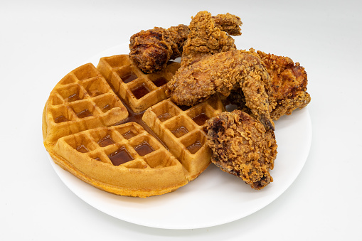 A portion of fried chicken with a Belgian style waffle with syrup on a white plate with a white background