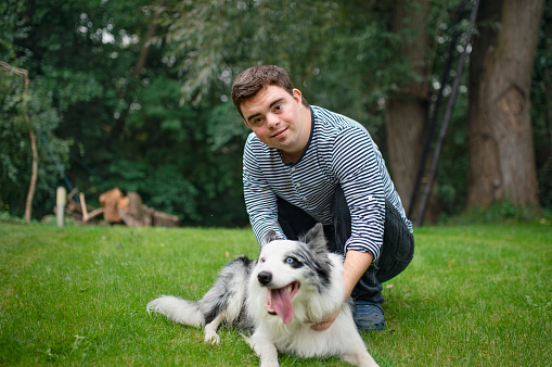 Portrait of cheerful down syndrome adult man playing with dog pet outdoors in backyard.