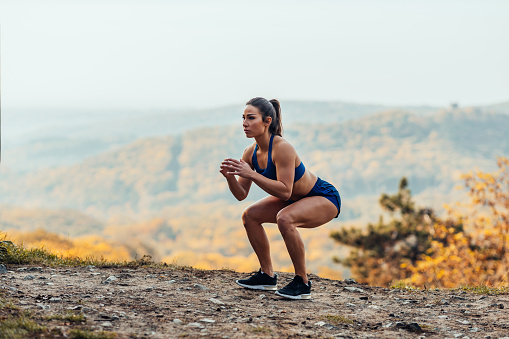 Shot of young athlete woman doing crouches outdoors.