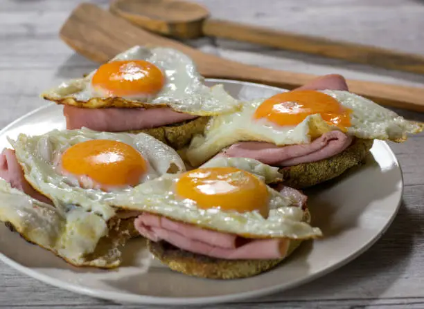 Fried eggs sunny side up with ham and toast served on a plate with rustic background
