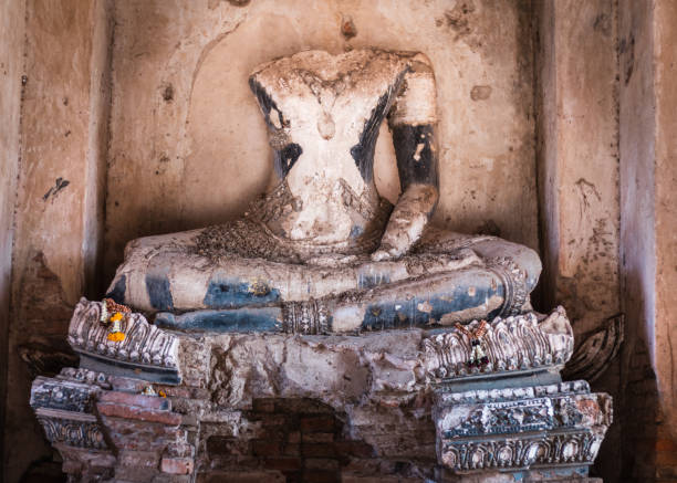 alte buddha-statue, kopflos und armlos. blumengirlande als opfergabe neben dem linken fuß. zerstörte und zerbrochene skulptur, antike ruinen in wat chaiwatthanaram, ayutthaya, thailand, südostasien - wat chaiwattanaram stock-fotos und bilder