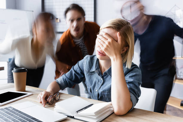 istock tired manager obscuring face with hand while sitting near notebook in open space office, motion blur 1288442042