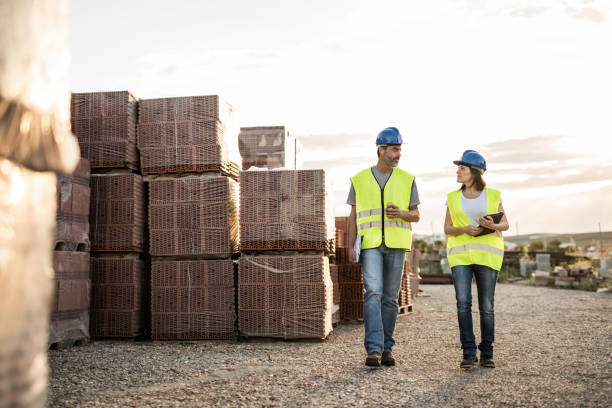 hombre y mujer, compañeros de trabajo de la construcción comen refrigerio y charlan amigablemente después de agotar el día de trabajo al atardecer cerca de ladrillos - amicably fotografías e imágenes de stock