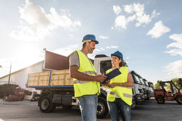 Two workers, a man and a woman, in a transport and construction company talk kindly about the destruction of work and material with the means of transport in the background. stock photo