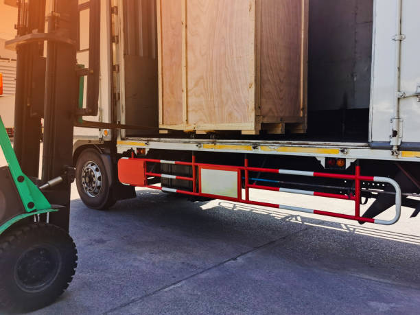 istock Worker driving forklift loading shipment carton boxes goods on wooden pallet at loading dock from container truck to warehouse cargo storage in freight logistics, transportation industrial, delivery 1288446217