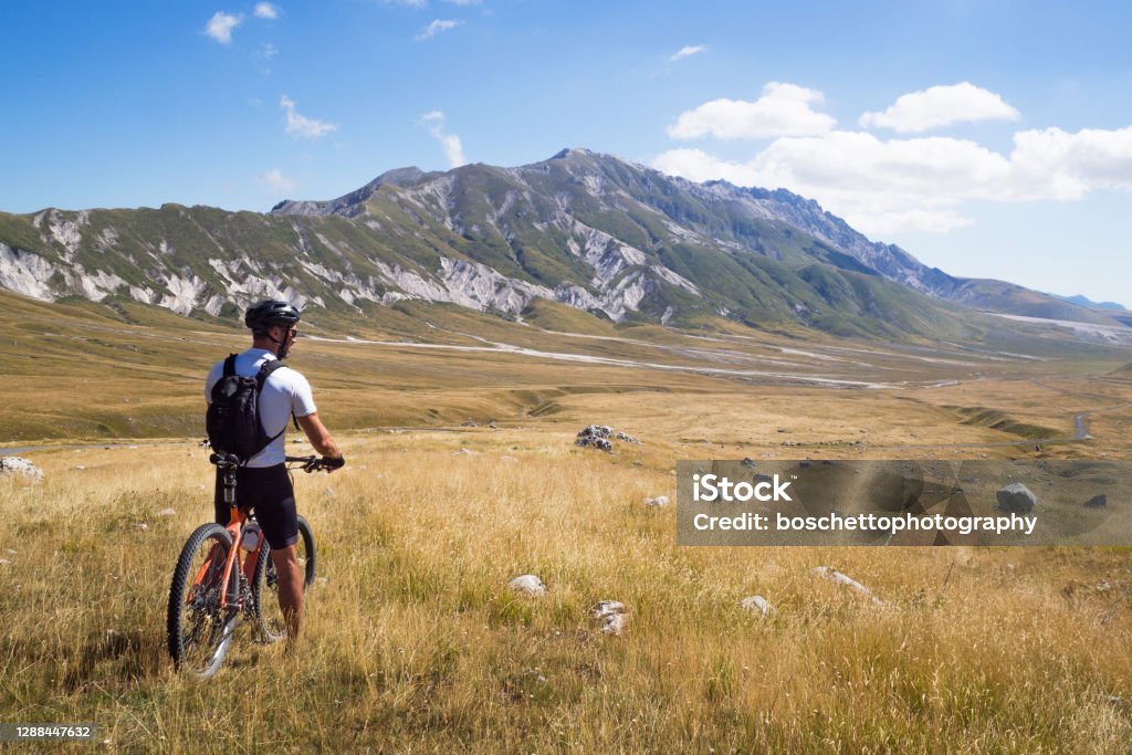 Mountain biker stopped on mountain trail with his bycicle enjoyng a panoramic view Adult mountain biker stopped on mountain trail with his bycicle enjoyng a panoramic view. Campo Imperatore, Abruzzo, Italy. Failure Stock Photo