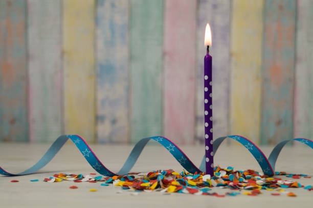 Birthday or party card composition. Birthday candle with paper ribbon and colorful confetti on a wooden table.