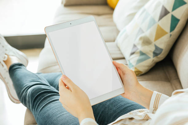 istock Tablet mockup held by a woman who is sitting on the couch. White screen 1288455696