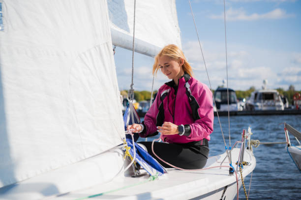 Women's river regatta on a sunny day. A young blonde sets up the rigging and secures the genaker sail before the start of the competition Women's river regatta on a sunny day. A young blonde sets up the rigging and secures the genaker sail before the start of the competition winch cable stock pictures, royalty-free photos & images