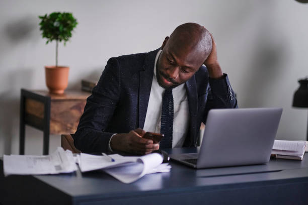 istock Young African executive reading documents and working on a laptop while sitting at his desk in an office. soft focus 1288457993
