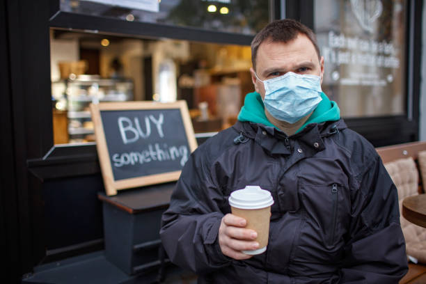 istock Man in medical mask standing before small cafe storefront with welcome sign on window 1288461931