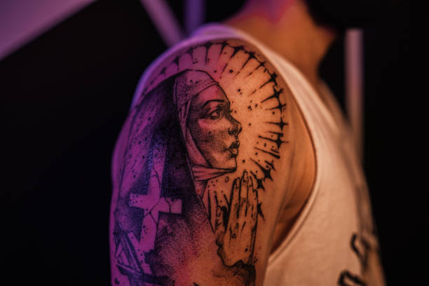 Tattoo woman, wearing a black mask, holding a tattoo machine, looking at the camera.