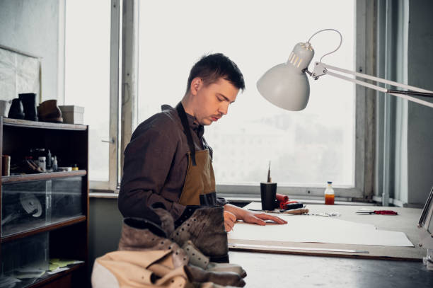 istock A young shoemaker makes a drawing for a pattern for leather shoes on a table in his workshop 1288467817