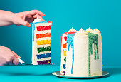 Woman taking a slice of cake. Homemade rainbow cake on blue background