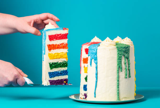 Woman taking a slice of cake. Homemade rainbow cake on blue background Woman's hands taking a slice of rainbow cake. Delicious homemade birthday cake against a blue background. gateau stock pictures, royalty-free photos & images