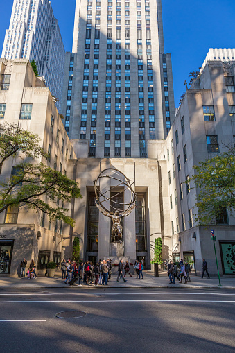 Rockefeller Center, Midtown Manhattan, New York, NY, USA. Rockefeller Center is a complex of commercial buildings  between 48th and 51st streets. It was declared a National Historic Landmark in 1987. Bronze Statue in the middle of the image depicts Atlas holding the heavens on his shoulders. It is within the International Building's courtyard. It is across Fifth Avenue from St. Patrick's Cathedral. Sightseeing tourists are walking around. Canon EF 24-105mm F/4L IS lens. Canon EOS 6D DSLR with full frame sensor.