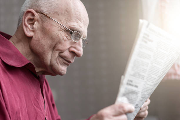 istock older man wearing glasses holding newspaper in hands and reading 1288472410