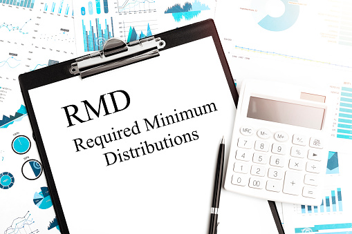 Text RMD Required Minium Distributions on clipboard. Calculator, pen, charts, documents and graphs on background.