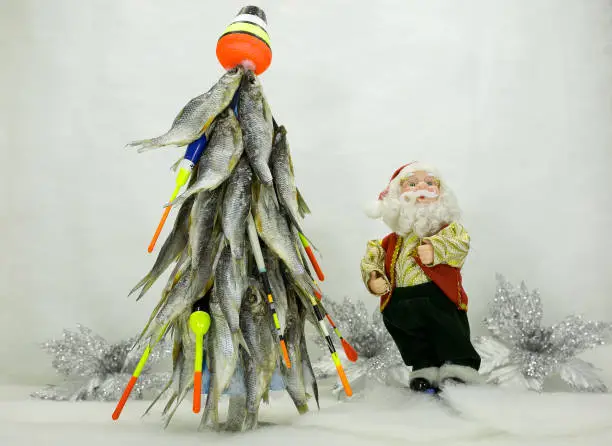 Photo of This Christmas tree is made of dried fish. New year for the fisherman. The tree is decorated with floats and fishing tackle. Cheerful Santa Claus near the Christmas tree.