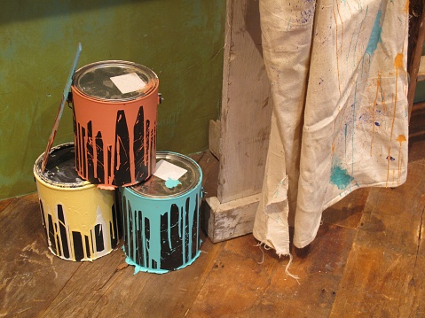 Orange, yellow and blue used paint cans with a drop cloth