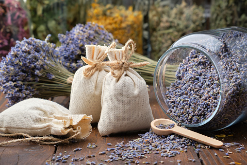 Glass jar of dry lavender flowers, sachets, bunches of dry lavender. Jars of different dry medicinal herbs on background. Alternative medicine.