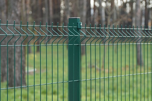 part of a green metal fence made of iron mesh on the street against the background of trees