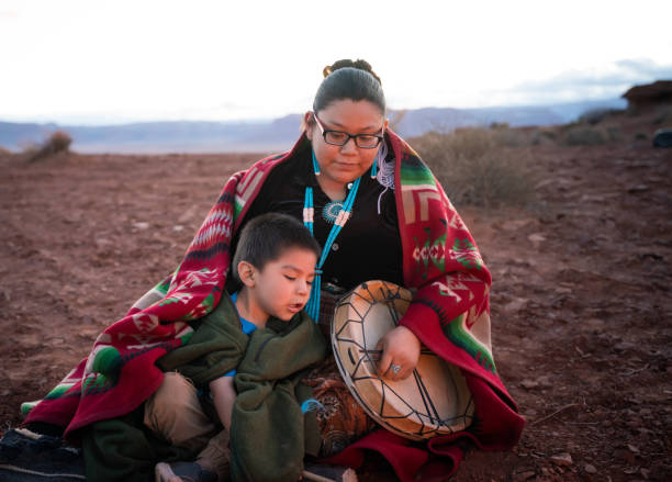 navajo junge frau hält eine traditionelle trommel mit kleinen bruder rund um lagerfeuer auf der wüste von arizona - navajo american culture indigenous culture women stock-fotos und bilder