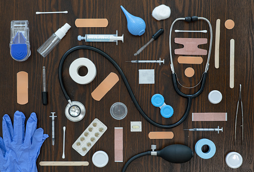 An array of medical tools and equipment is displayed on a wooden surface and pictured from above.